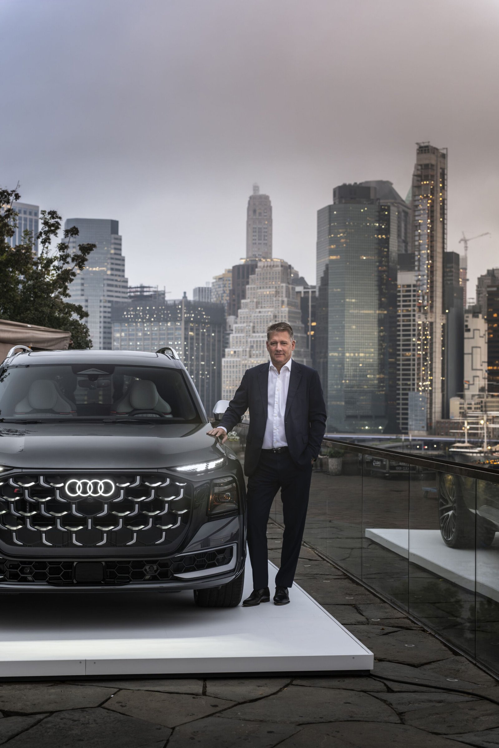 Audi CEO Gernot Dollner standing beside the Q9 SUV with the New York skyline behind him