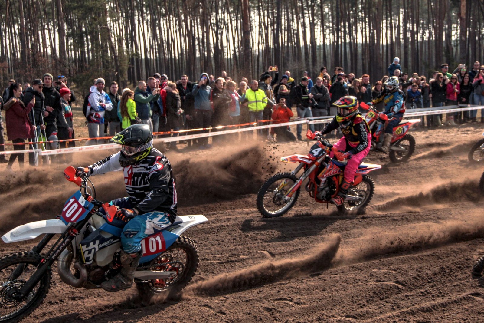 Two motocross riders racing side by side on a dirt track in front of spectators
