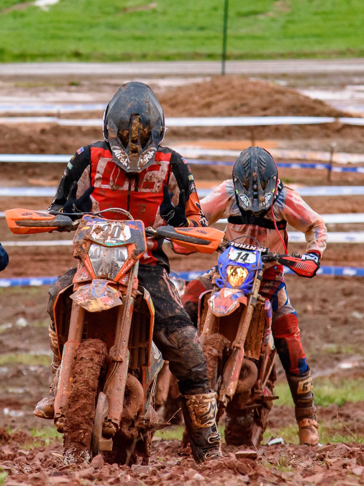 Two motocross riders covered in mud stopped on a dirt track
