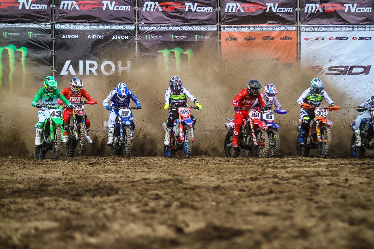 Row of motocross riders at a dust-filled stadium starting gate
