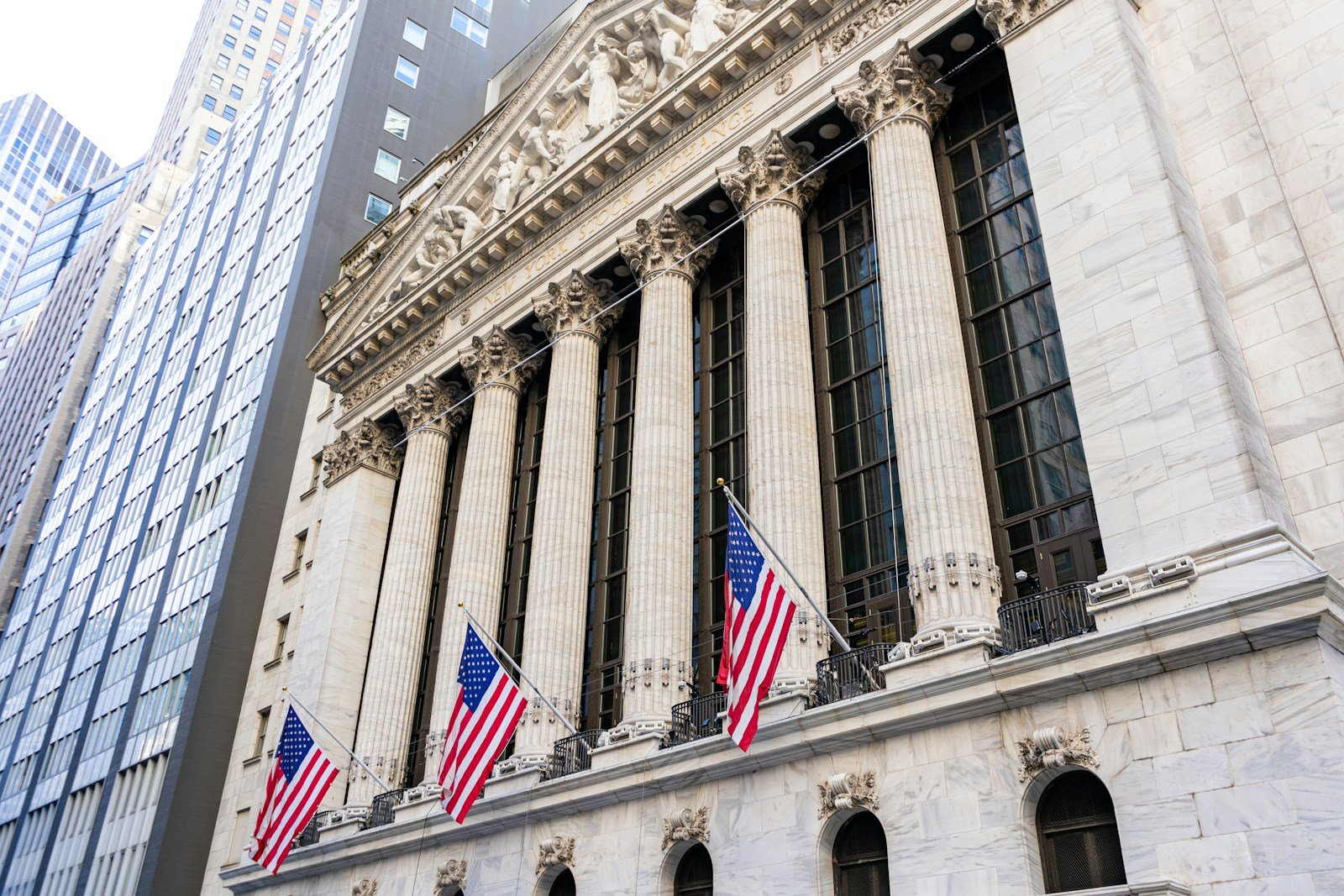 The columned facade of the New York Stock Exchange building with American flags hanging between the pillars