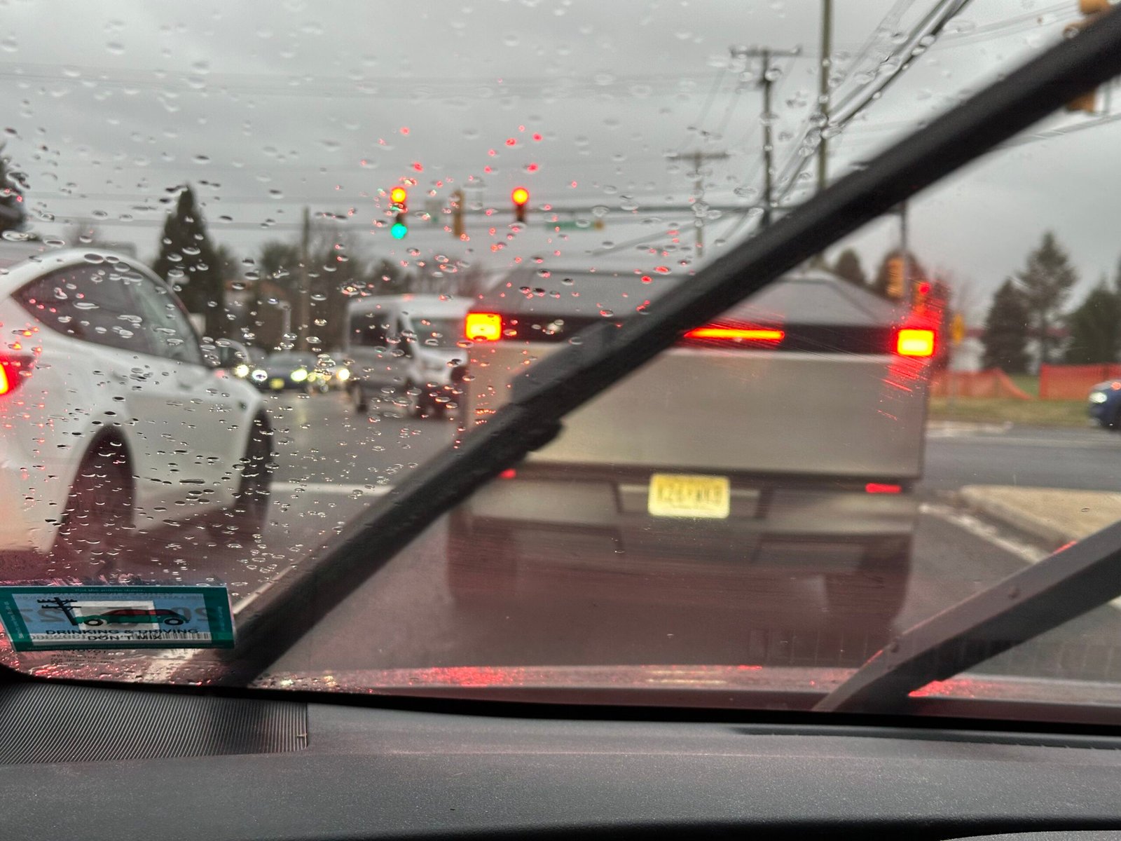 A Tesla Cybertruck waiting in traffic as seen through a rain-streaked windshield