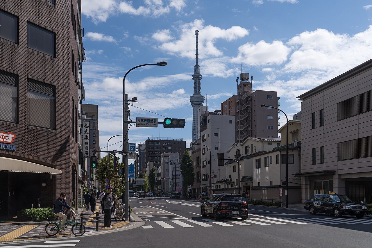 A busy Tokyo street with a taxi, cyclist and pedestrians, with Tokyo Skytree in the background