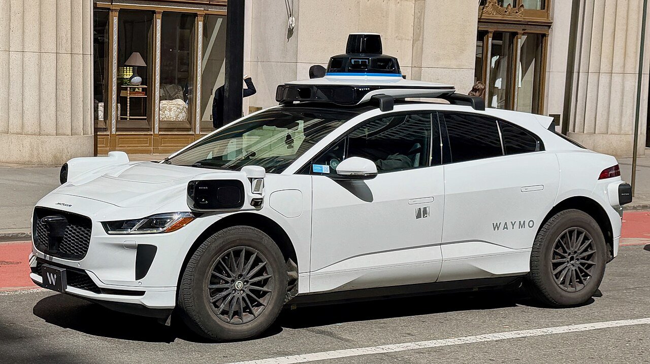 A white Waymo self-driving Jaguar I-Pace with visible sensor pods parked on a city street